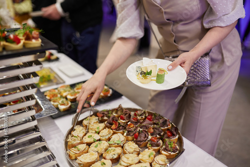 Close-up of people putting snacks on a plate during a banquet at a beautifully set table with a white tablecloth