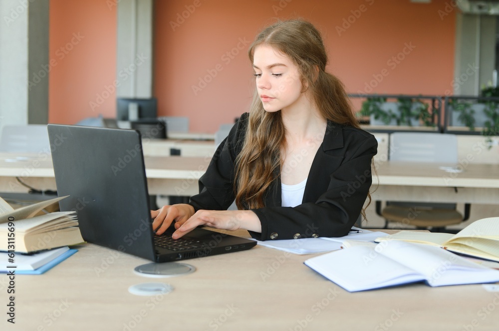A beautiful caucasian female student is studying in college remotely. She is sitting with a laptop and a notepad and concentrated is watching a video conference lesson A beautiful caucasian female student is studying in college remotely. She is sitting with a laptop and a notepad and concentrated is watching a video conference lesson