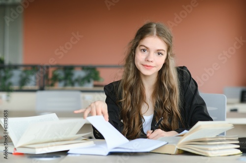 Teen girl studying with textbook writing essay learning in classroom.