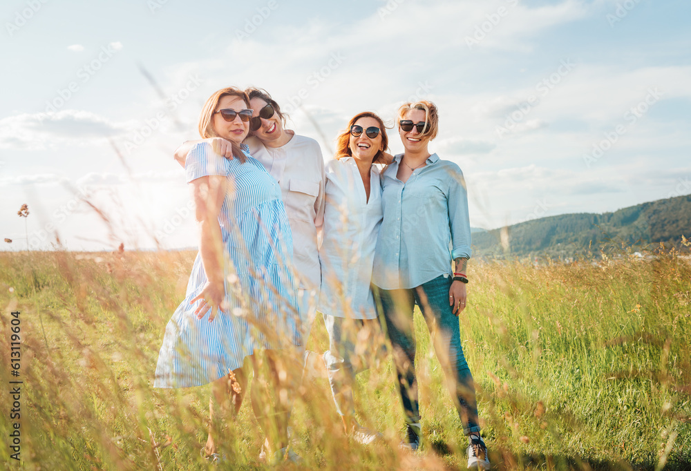 Portrait of four cheerful smiling and laughing women embracing during outdoor walking by high green grass hill. They looking at the camera. Woman friendship, relations, and happiness concept image. Portrait of four cheerful smiling and laughing women embracing during outdoor walking by high green grass hill. They looking at the camera. Woman friendship, relations, and happiness concept image.