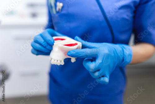 Crop unrecognizable female dentist in uniform and latex gloves holding dental plaster model in light modern clinic