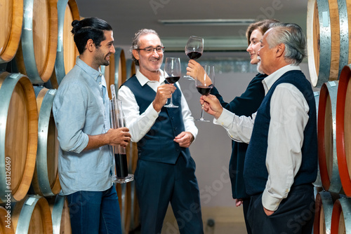 Professional male sommelier explaining and recommending wine to customer and visitors at wine cellar with wooden barrel in wine factory. Winery liquor manufacturing industry and winemaker concept.
