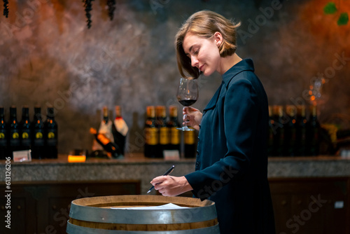 Canvastavla Professional woman sommelier testing red wine in wine glass with tasting and smelling at wine cellar with wooden barrel in wine factory
