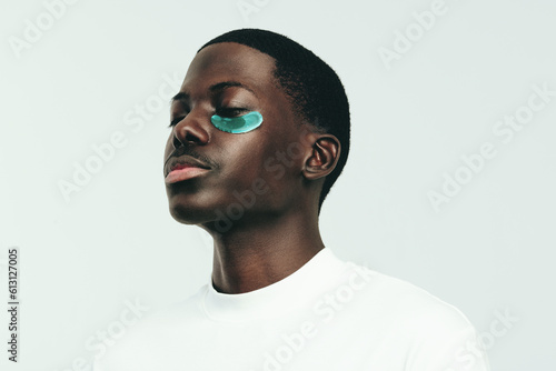 Tela Man with melanin skin indulging in some under eye care with a hydrogel patch