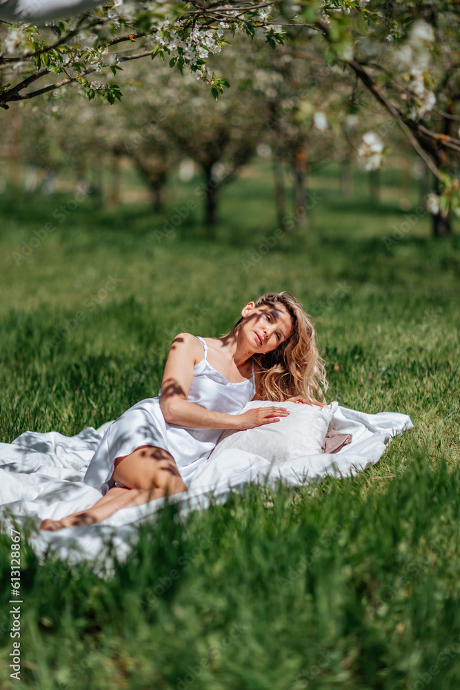 woman sleeps on a white bed in the fresh spring grass in the garden. Dressed in a blue nightgown. woman sleeps on a white bed in the fresh spring grass in the garden. Dressed in a blue nightgown.