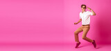 Photo of a dancing man on summer vacation, active, wearing shirt, pants, shoes, sunglasses, isolated on a pink background. text copyspace banner background. Generative ai