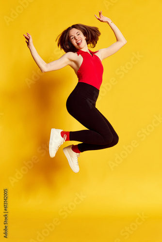 Full-length portrait of young beautiful girl in casual clothes cheerfully jumping against yellow studio background. Happy and delightful. Concept of youth, human emotions, lifestyle, ad