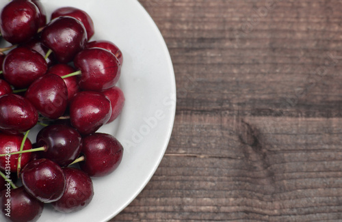 Cherries in a white plate on a wooden table