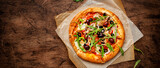 Pizza with salami sausage, mozzarella cheese, mushrooms, black olives, spicy tomato sauce and arugula, rustic wooden table background, top view banner with copy space