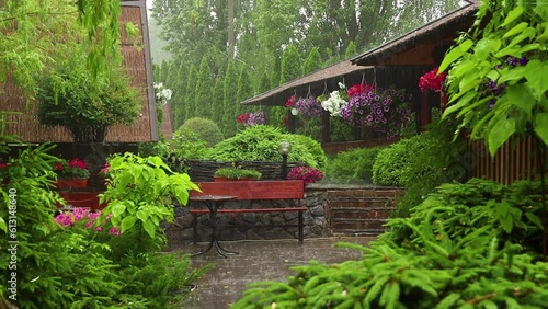 Rain in a picturesque backyard garden with flowers, a bench and a table in summer