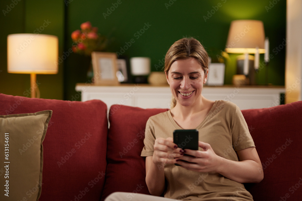 Happy woman text messaging on mobile phone while relaxing on sofa at home Happy woman text messaging on mobile phone while relaxing on sofa at home