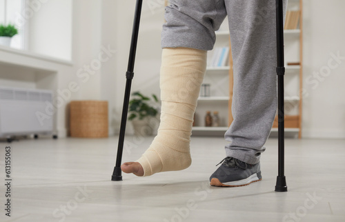 Tableau sur toile Man with broken leg in cast walking with crutches at home