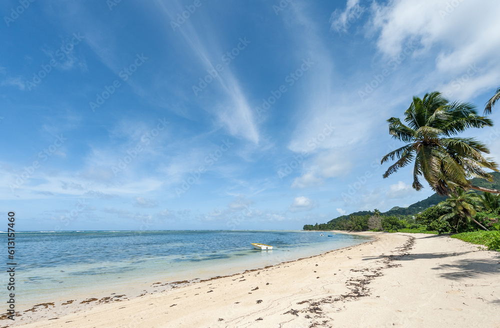 Beach in Seychelles with Ocean Water and Blue Sky with Clouds. Landscape. Low Tide Water. Boats in Background.