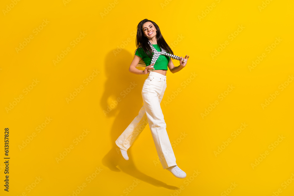 Full length photo of shiny excited lady wear white pants jumping high tying sweater empty space isolated yellow color background Full length photo of shiny excited lady wear white pants jumping high tying sweater empty space isolated yellow color background
