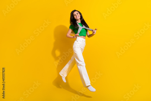 Full length photo of shiny excited lady wear white pants jumping high tying sweater empty space isolated yellow color background