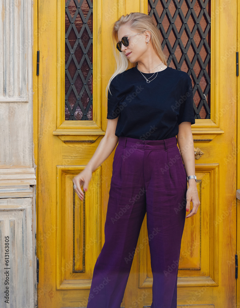 Young blond beautiful model is posing next to a yellow door in a cool city wearing a black t-shirt. Young blond beautiful model is posing next to a yellow door in a cool city wearing a black t-shirt.