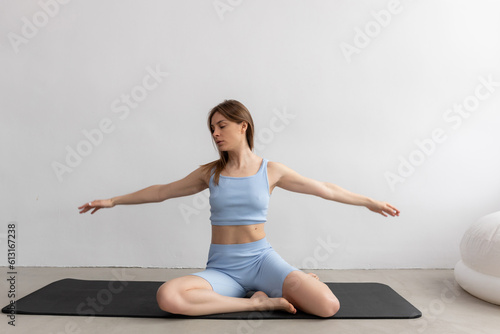 Portrait of young concentrated toned woman doing exercise, stretching hands, practising yoga, sitting on black mat.