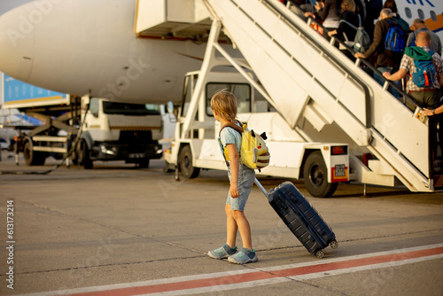 Cute blond child, kid with backpack, boarding airplane at the airport on sunset, enjoying the view