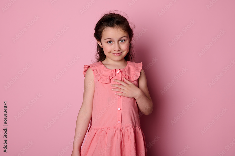 Studio portrait of beautiful authentic shy little child girl 5-6 years old, dressed in elegant pink dress, smiling cutely looking at camera, isolated pink background. Happy carefree childhood concept Studio portrait of beautiful authentic shy little child girl 5-6 years old, dressed in elegant pink dress, smiling cutely looking at camera, isolated pink background. Happy carefree childhood concept