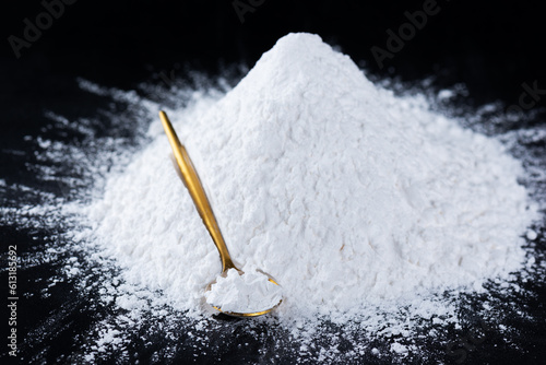 Heap of tapioca starch powder with spoon on a black background, dry cassava root.