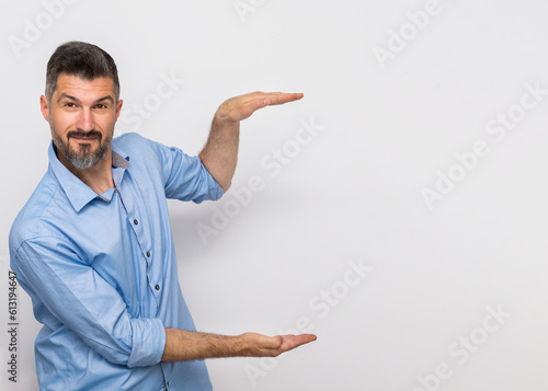 Happy adult smiling professional business man wearing blue shirt looking at camera pointing finger away at copy space showing aside presenting advertising offer standing isolated at gray.