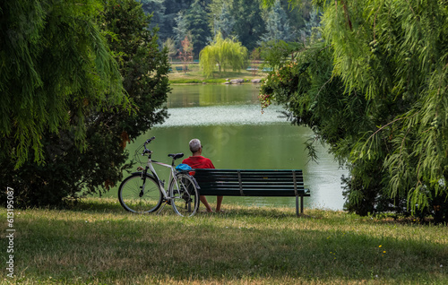 man sitting on bench in park and looks at lake