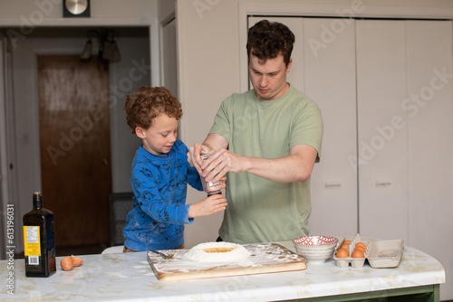 A father and son looking busy while putting some salt into the fresh pasta dough for dinner.