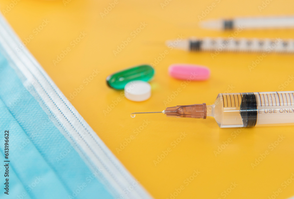 The mask is light blue and syringe have red and green pills on yellow background