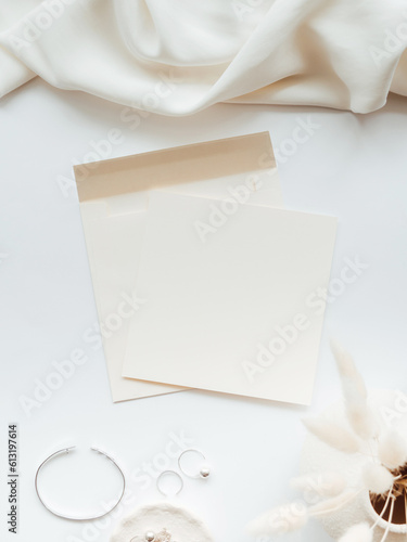 White blank paper sheet card mockup, envelope and floral branch in vase and silver jewelry on white background.
