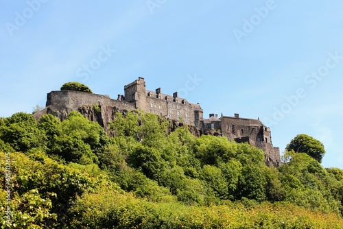 A full view of Stirling castle in the distance from below sitting atop the hill surrounded by trees