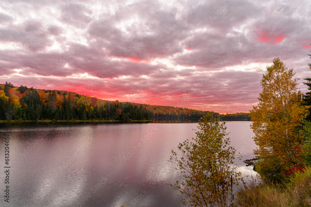 Dramatic sunset sky over a lake surrounded by forested hills at the peak of autumn colours