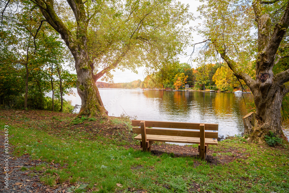 Empty wooden bench facing a beutiful lake with wooded shores at the peak of fall foliage. Concept of loneliness. Empty wooden bench facing a beutiful lake with wooded shores at the peak of fall foliage. Concept of loneliness.