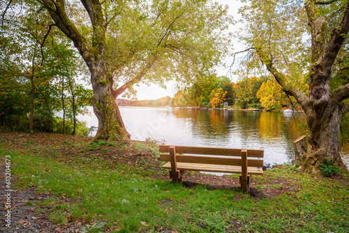 Empty wooden bench facing a beutiful lake with wooded shores at the peak of fall foliage. Concept of loneliness.