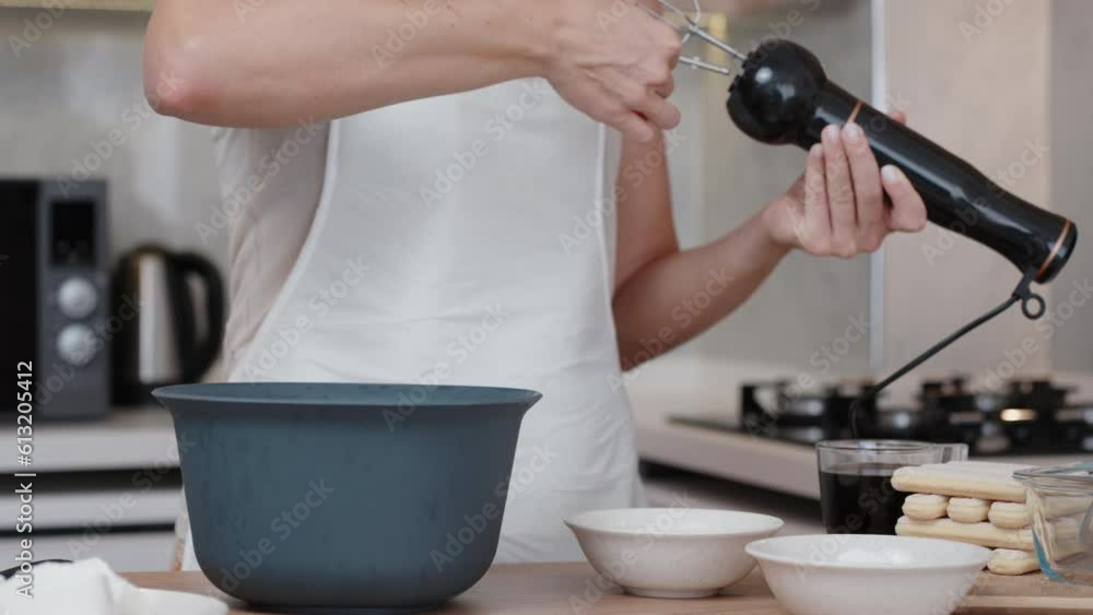 The woman inserts whisk attachments into a hand blender and pours something white into a bowl.