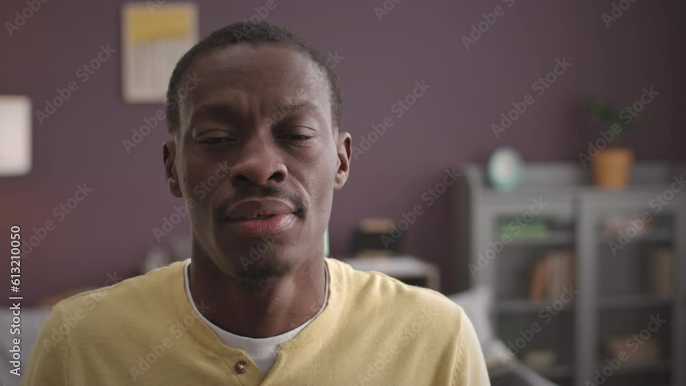 Chest up slowmo portrait of confident young Black man raising his head up at camera standing in purple walled room in blurred background Chest up slowmo portrait of confident young Black man raising his head up at camera standing in purple walled room in blurred background