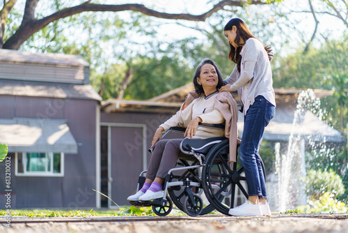 Asian senior woman in wheelchair with happy daughter. Family relationship retired woman sitting on wheelchair in the park age care at retirement home.