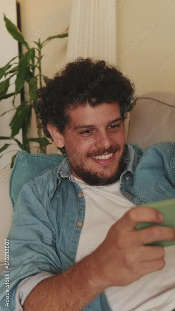 Smiling guy gamer plays video games with mobile phone lying on sofa Smiling guy gamer plays video games with mobile phone lying on sofa