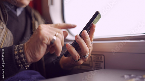Close-up of the hands of an senior sitting in a train carriageriage and using a smartphone