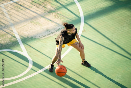 Brutal woman dribbling basketball ball on court