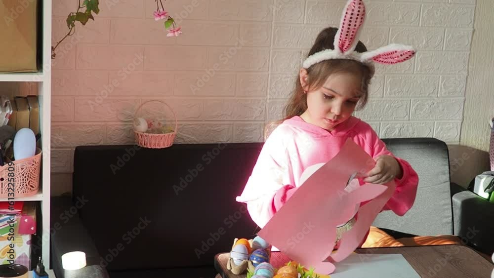 a little cute girl in a pink dress cuts out hares from paper at home ...