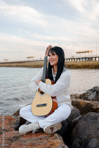 young girl with a guitar on the pier rocks in the sea (ID: 613226034)
