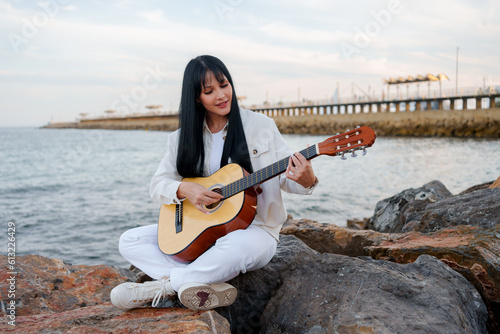 young girl with a guitar on the pier rocks in the sea (ID: 613226429)
