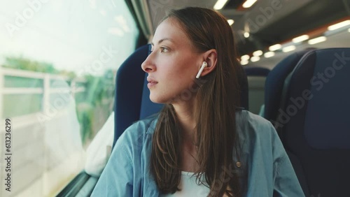 Cute girl with long brown hair, wearing blue shirt, wearing wireless earphone into ear traveling by suburban train photo