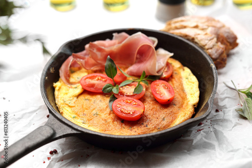 Fresh french omelette with tomato and prosciutto on a cast iron pan, with blurred background.