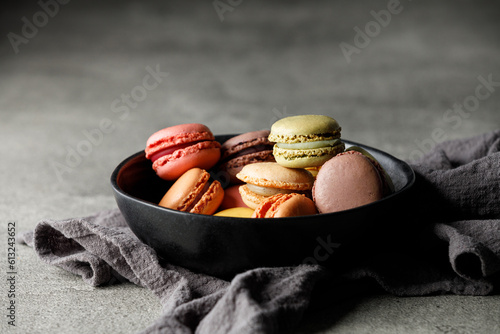 Different macaroons in a black bowl on a towel. Black background, close-up, free space for text	
