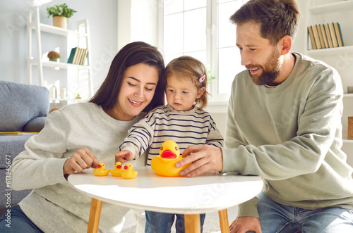 Dad  mom and toddler baby playing toys at home. Cheerful caring parents and kid playing with rubber duck toys together in living room at home. Happy parenthood  childhood concept