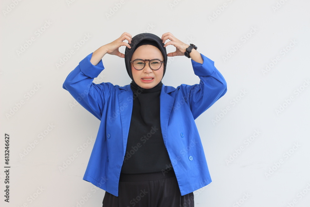 beautiful young asian muslim woman, wearing glasses and blue blazer is angry holding her head beautiful young asian muslim woman, wearing glasses and blue blazer is angry holding her head