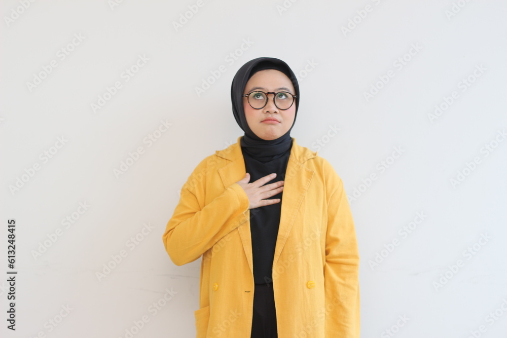 Beautiful young Asian Muslim woman in glasses and smiling putting both hands on chest and showing affection gesture isolated over white background Beautiful young Asian Muslim woman in glasses and smiling putting both hands on chest and showing affection gesture isolated over white background