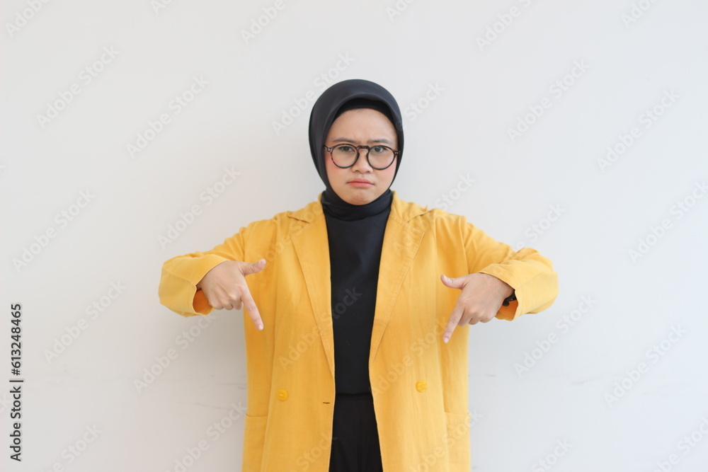 Beautiful young Asian Muslim woman in glasses, hijab and wearing yellow blazer sad expression with both hands pointing down Beautiful young Asian Muslim woman in glasses, hijab and wearing yellow blazer sad expression with both hands pointing down