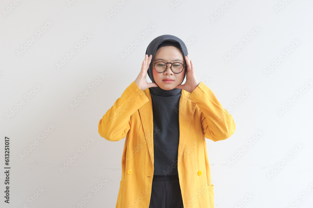 beautiful young Asian Muslim woman, wearing glasses and yellow blazer with dizzy expression holding head beautiful young Asian Muslim woman, wearing glasses and yellow blazer with dizzy expression holding head